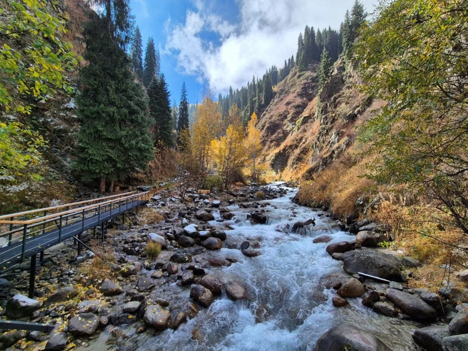 A wooden boardwalk running alongside Alma-Arasan's rushing gorge stream in autumn