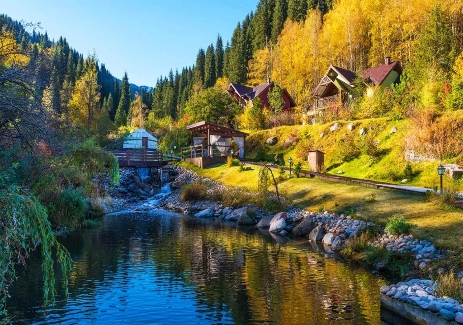 A mountain stream lined with cabins and a yurt at Oi-Qaragai in autumn