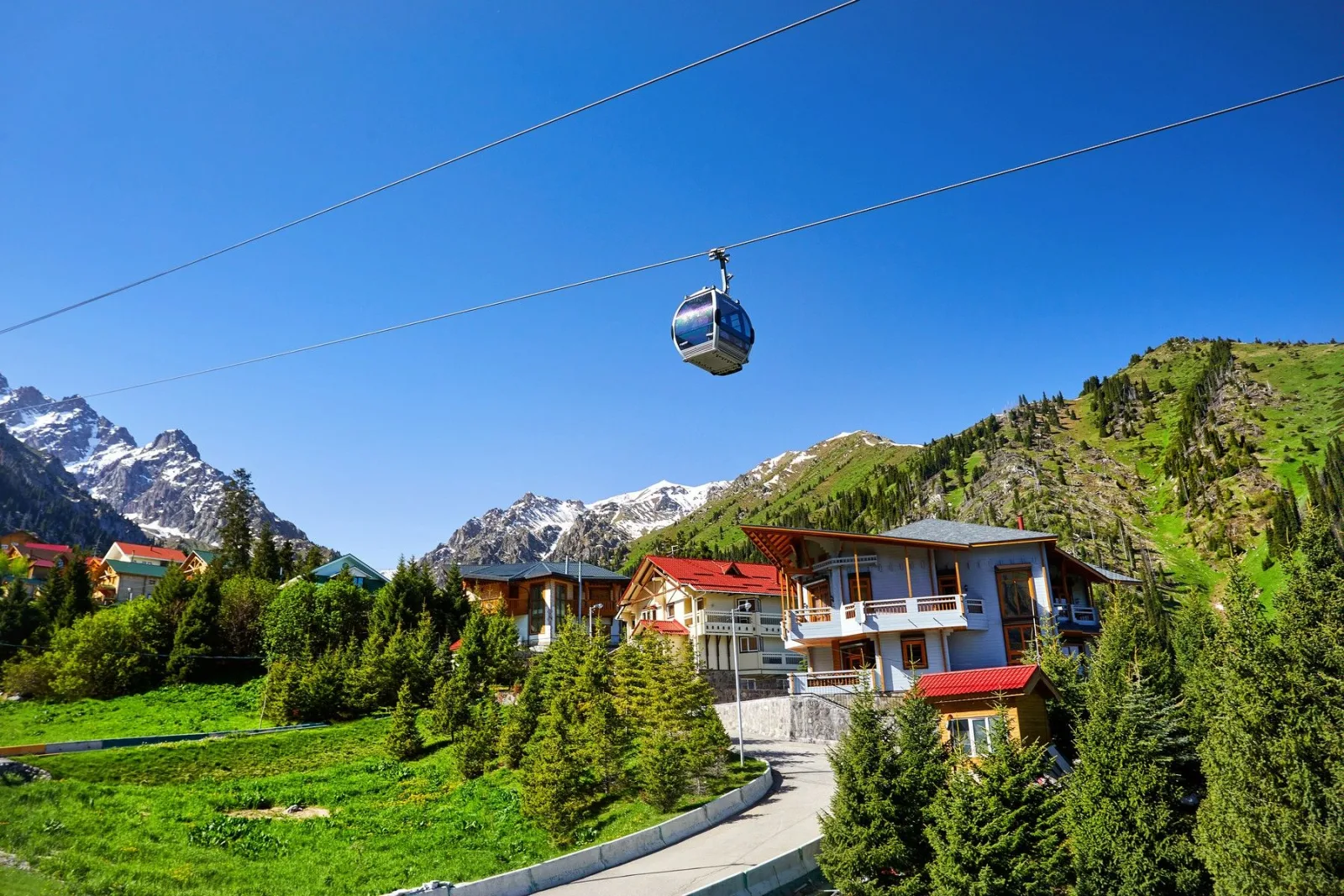 A gondola cabin gliding over Shymbulak's chalet village with snow-capped peaks behind