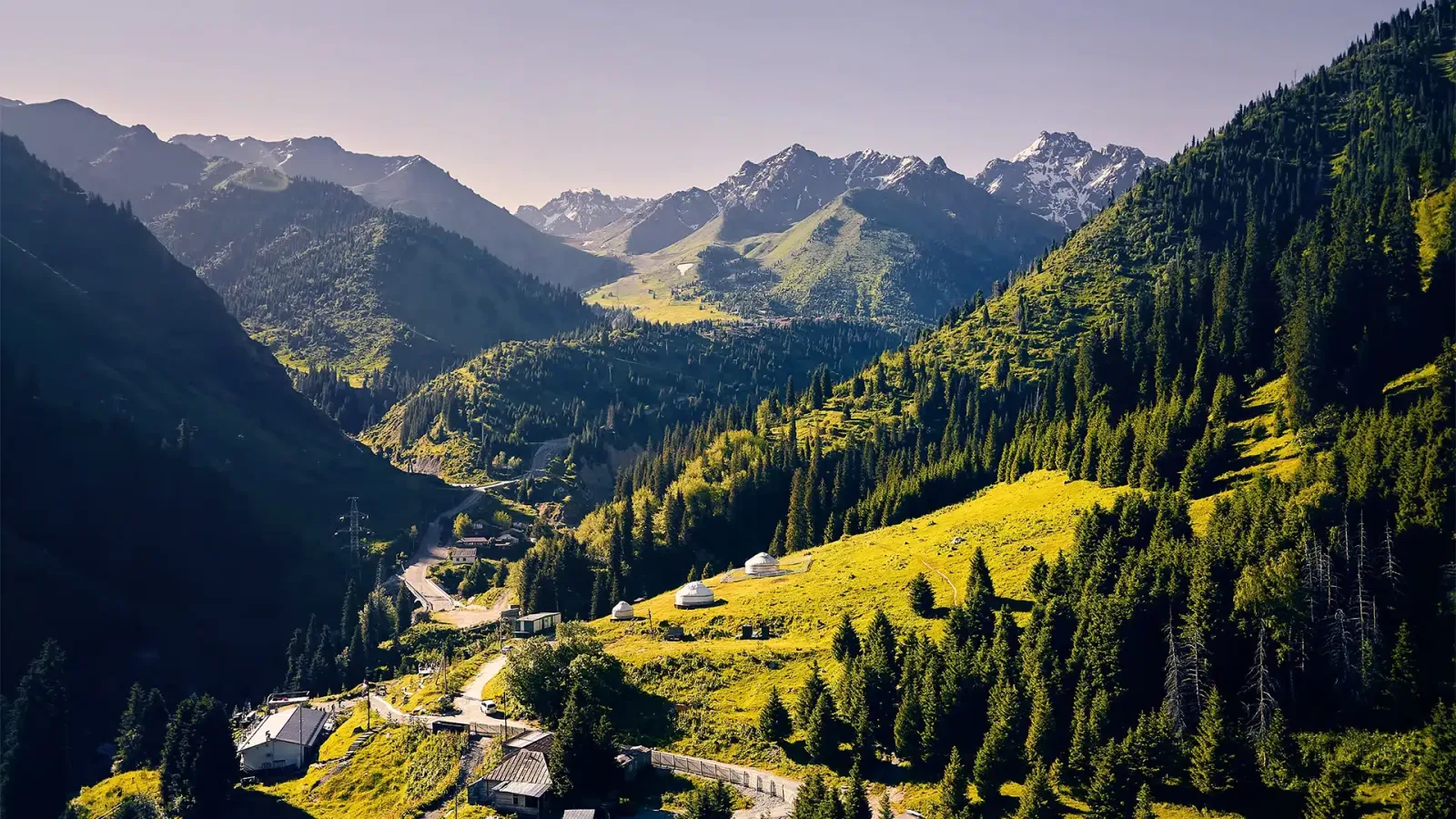 Aerial view of the road winding up to Shymbulak past yurts and forested slopes