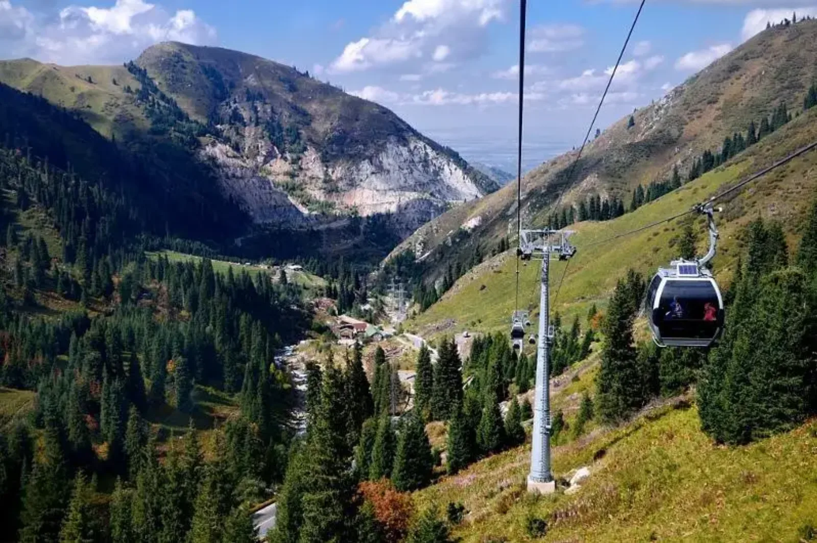 A gondola cabin descending into the pine-forested valley at Shymbulak